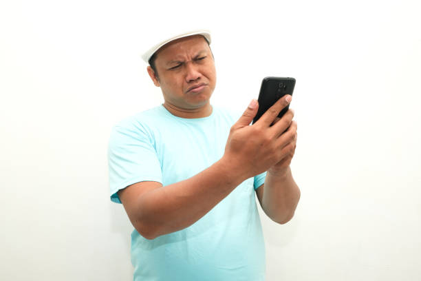 istock Adult Asian man thinking about something while holding mobile phone 2156985149