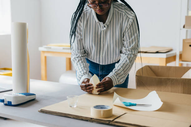 istock Woman Packing Items in a Cardboard Box in a Workspace 2156987509