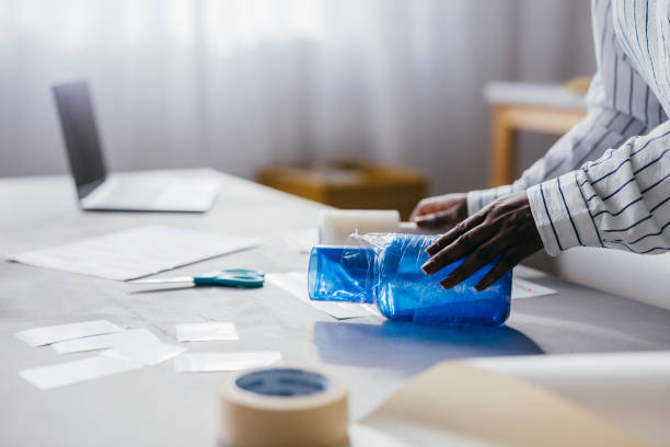 istock Person Wrapping Blue Plastic Bottle in Plastic Film at a Desk 2156987594