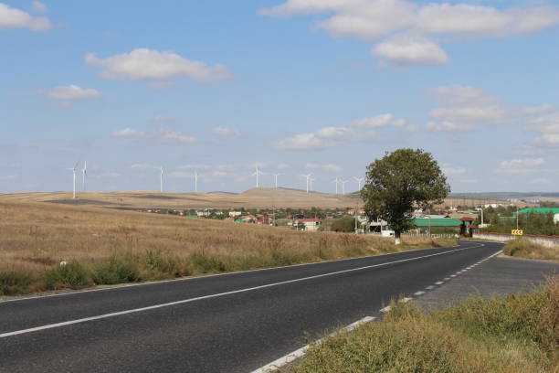 A road with a road and windmills in the background. Road. Outdoor. Grass. Sky. Way