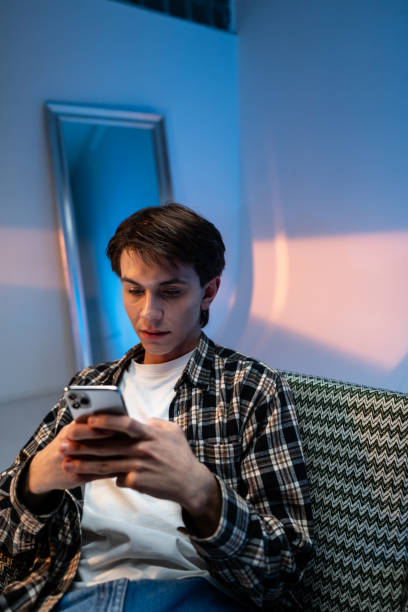 istock Young guy sitting in a armchair and browsing on her mobile phone at the studio 2156994381