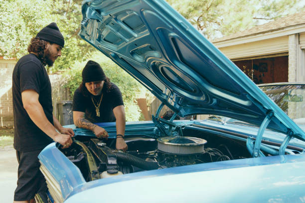 Young hispanic men working on a vintage lowrider car in a home driveway.