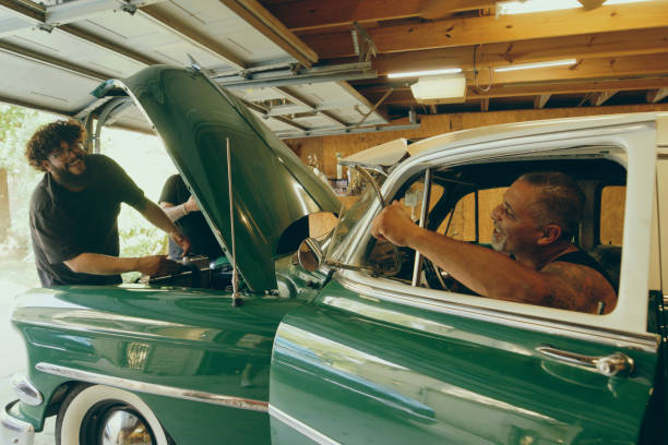 A hispanic father and sons working on a vintage car in a home garage.