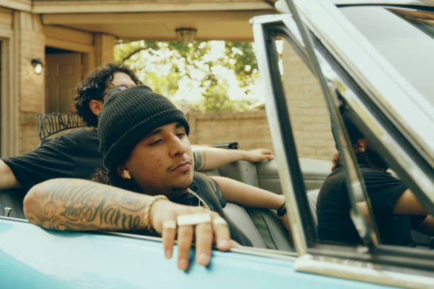 Three young hispanic men in a lowrider convertible vintage car, driving out of the garage driveway.