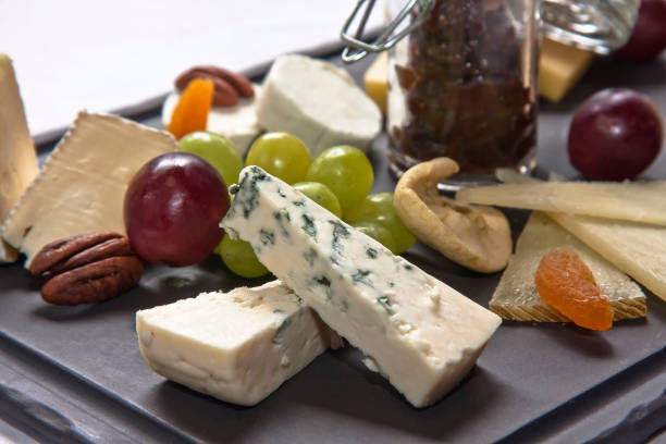 Cheese board. Assortment of cheeses with nuts, bread, grapes, fruit in syrup on stone slate plate. White background
