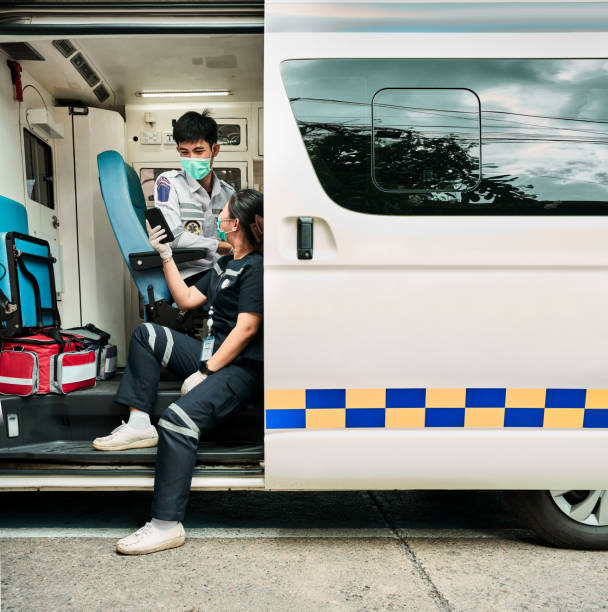 Two paramedics sitting in the ambulance outside using mobile phone while on standby for a call