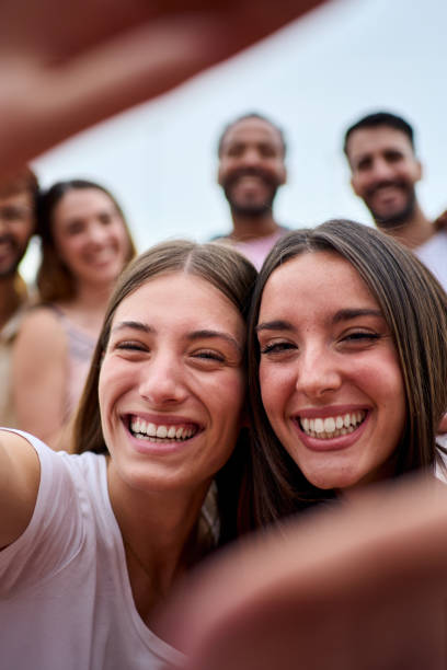 istock Two girl friends making a frame with hands. Unfocused group young people are taking selfie together. 2157007205