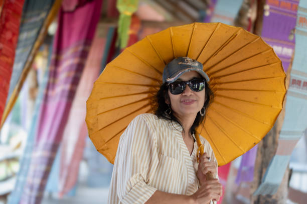 Portrait of middle-aged asian woman holding umbrella standing in front of woven fabric which was decorated of the local cafe.