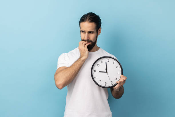 istock Man sitting biting her nails holding big wall clock, deadline, afraids to be late. 2157015107