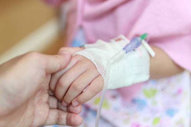 Mother holding child hand with saline IV solution in hospital