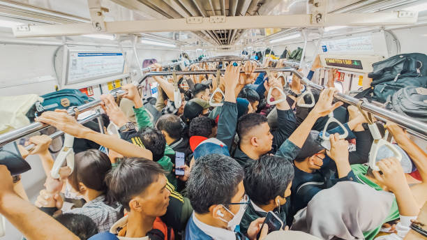 Depok, West Java, Indonesia. June 10, 2024. High angle view. Group of adults standing uncomfortably close together into a crowded commuter train. The commuter train is a major component of the railway system in Indonesia