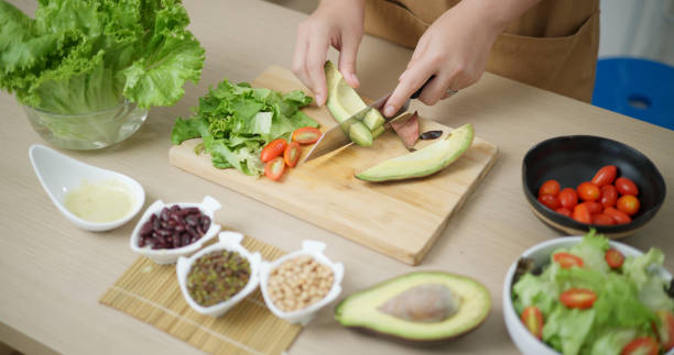 istock Young woman's hands cutting avocado to make salad. 2157033144