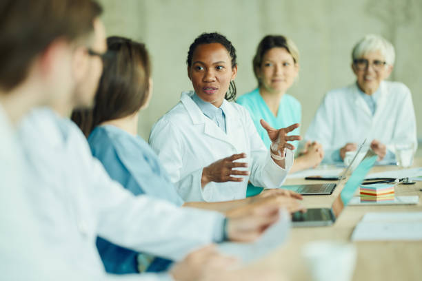 Black female doctor talking to her colleagues on a meeting in hospital. African American female doctor communicating with her colleagues during a meeting in hospital. medical occupation stock pictures, royalty-free photos & images