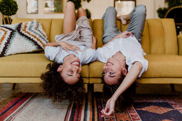 istock Cheerful women lying upside down on a mustard yellow couch 2157053837