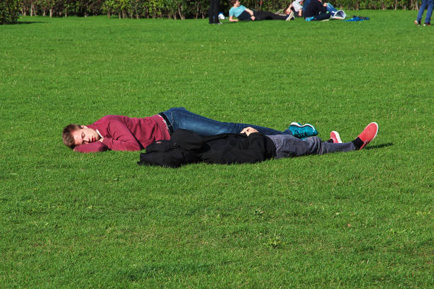 A young woman lies comfortably on her back atop a stone wall in a natural outdoor setting. She appears peaceful and relaxed. Surrounded by lush greenery, the scene conveys a mood of calmness, solitude, and connection with nature. Mental wellness, relaxation, freedom, and mindful living.