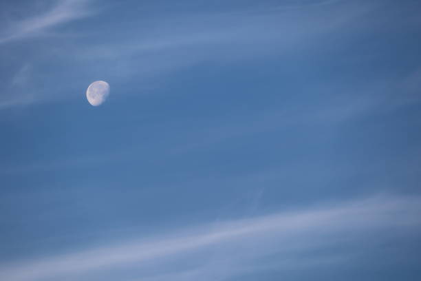Daytime moon embraced by soft clouds in the blue sky, creating a tranquil and peaceful scene in nature