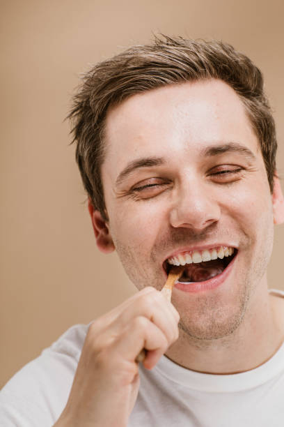 istock Blond man brushing his teeth with a wooden toothbrush 2157057218