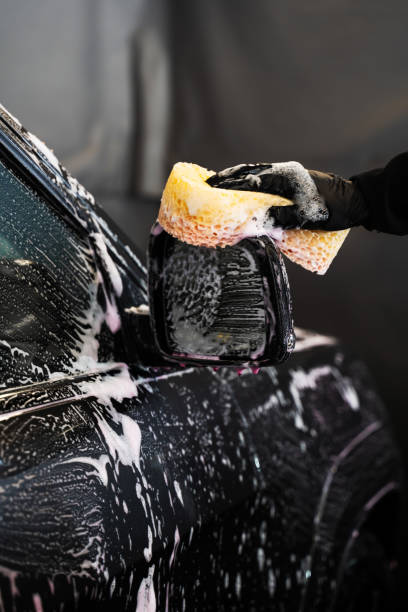 istock Cleaning the vehicle side mirror using sponge and pink foam detergent during a manual vehicle washing at a self-service car wash. 2157057774
