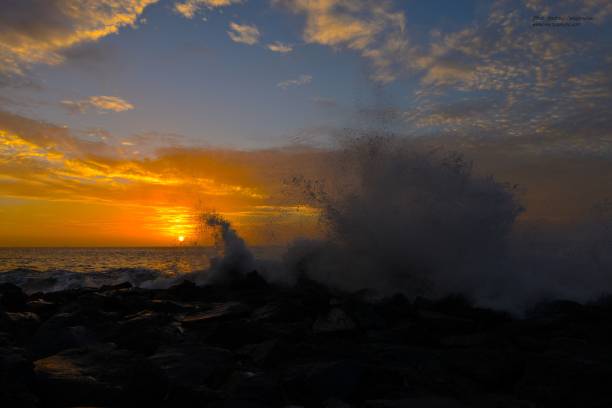 The splashing waves and coastal rocks at vibrant sunset. Spain