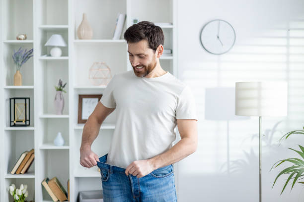 istock Man proudly showing weight loss in casual home setting 2157067471