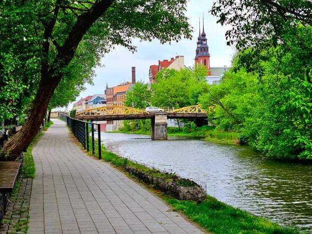 A scenic pathway by the river with a bench and bridge in the distance