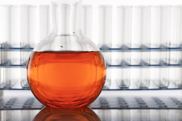 Close up of a glass beaker with red-orange liquid standing on a laboratory countertop and backlit.