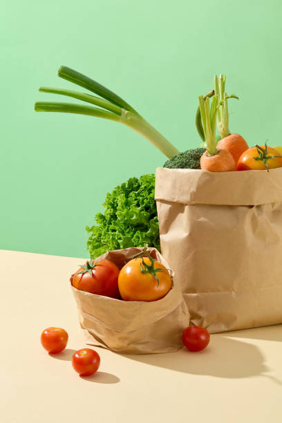istock Fresh vegetable ingredient for cooking contained in brown paper bag, placed on yellow kitchen counter, against green background. Blank space for designing and adding text 2157071300