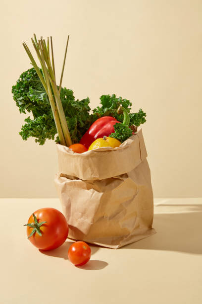 istock Plenty vegetables ingredients contained in brown paper bag displayed on yellow table, next to a few ripe tomatoes and cherry tomatoes. Blank space for text, front angle 2157072093