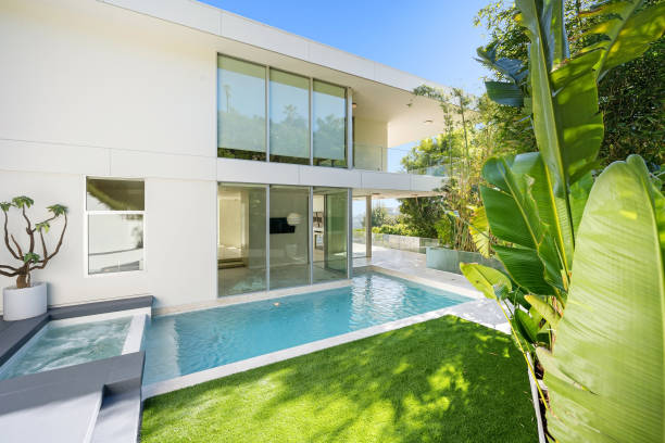 A small pool beside a luxurious white modern house surrounded by plants