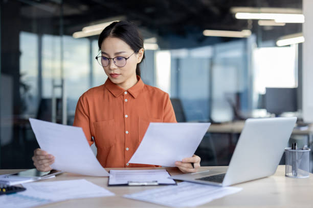 istock Asian financial woman working inside office with documents, papers behind paperwork, serious businesswoman looking financial reports at workplace , confident successful female accountant 2157077192