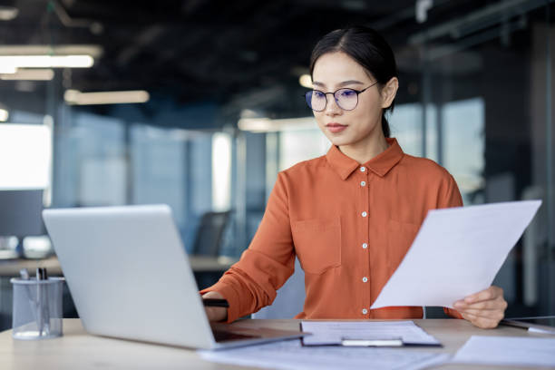 istock Asian financial woman working inside office with documents, papers behind paperwork, serious businesswoman looking financial reports at workplace , confident successful female accountant 2157078110