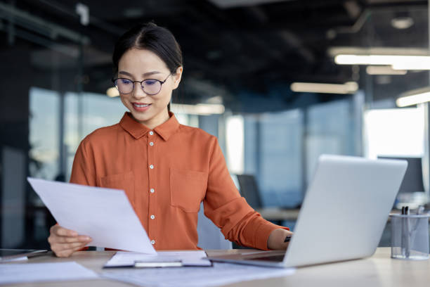 istock Asian successful smiling financier inside office working on paper work, businesswoman reviewing contracts and reports, worker using laptop, accountant auditor checking financial indicators data 2157079680