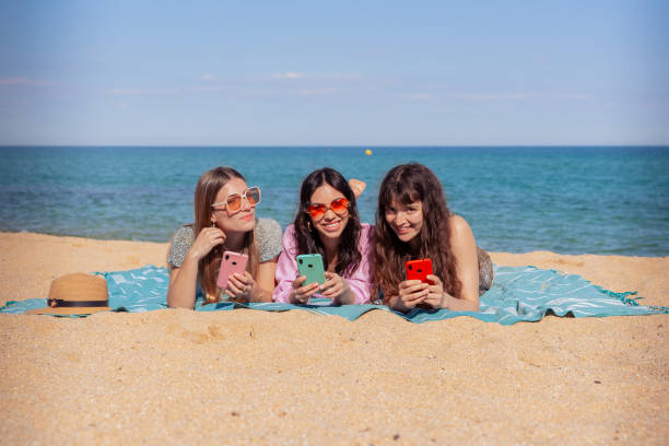 istock Three happy young friends on the beach using apps on their smartphones 2157080319