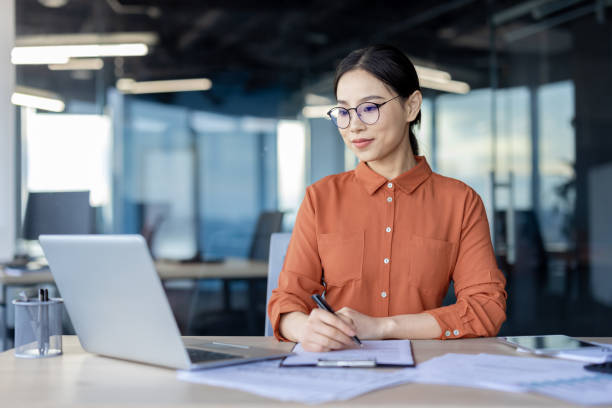 istock Asian businesswoman working on laptop taking notes in modern office 2157081598