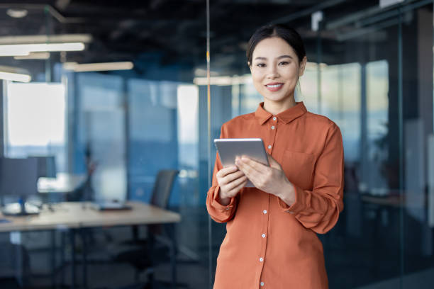 istock Portrait of a successful Asian female programmer with a tablet computer in her hands, an employee of a development company is smiling and looking at the camera near the window 2157082313