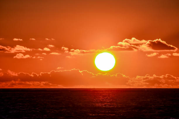 The sun is setting over the ocean, casting a warm glow on the water. The sky is filled with clouds, creating a serene and peaceful atmosphere, image