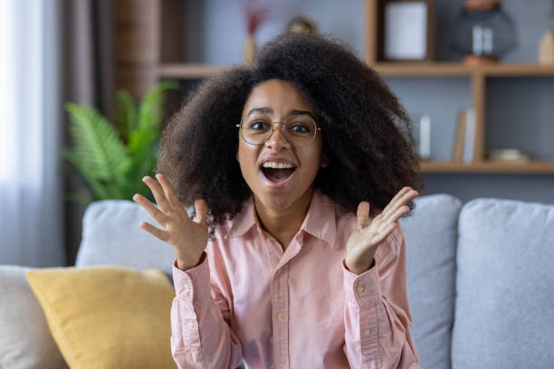 istock Excited woman expressing surprise and joy while sitting on a cozy couch indoors 2157084772