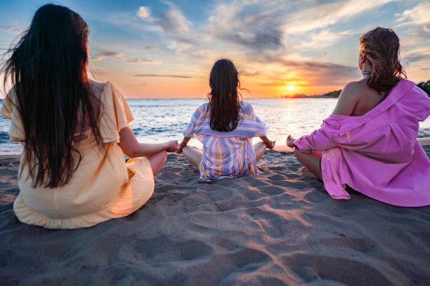 Rear view of a relaxed women meditating at the beach during sunset