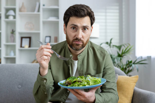 istock Man looking confused while holding a plate of salad at home 2157089490