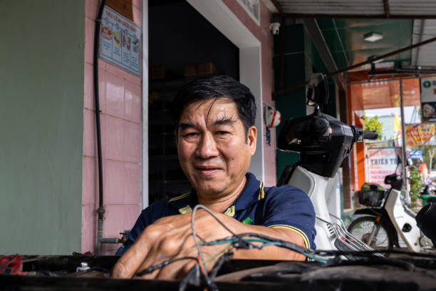 Portrait of an Asian man with long black eyebrows. He is looking at the camera while he is in his workshop working. Portrait of an Asian man with long black eyebrows. He is looking at the camera while he is in his workshop working. vietnamese old man portrait stock pictures, royalty-free photos & images