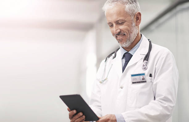 istock Senior doctor, man and reading tablet with app, happy and thinking for solution in corridor at hospital. Mature medic, person and touchscreen for telehealth with smile for results, ideas and vision 2157091622