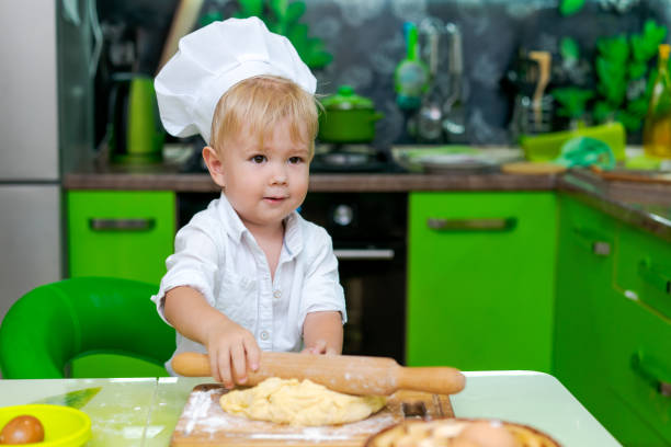 istock happy little boy preparing dough in kitchen at table. there are dough products on table, dressed as chef 2157093328