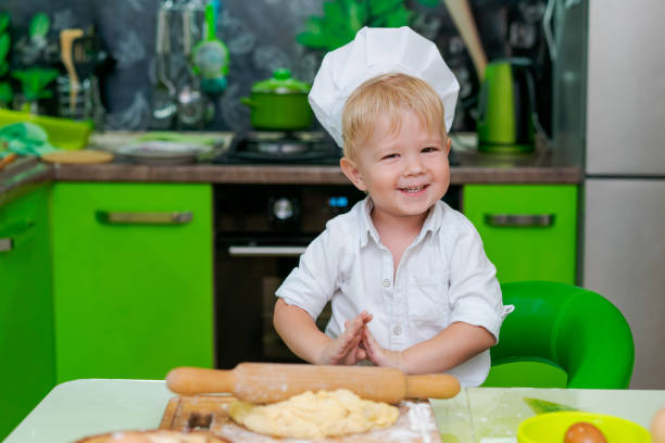 istock happy little boy preparing dough in kitchen at table. there are dough products on table, dressed as chef 2157093335