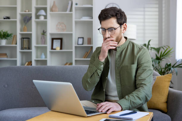 istock Man working from home on laptop, thinking and analyzing in modern living room 2157094919