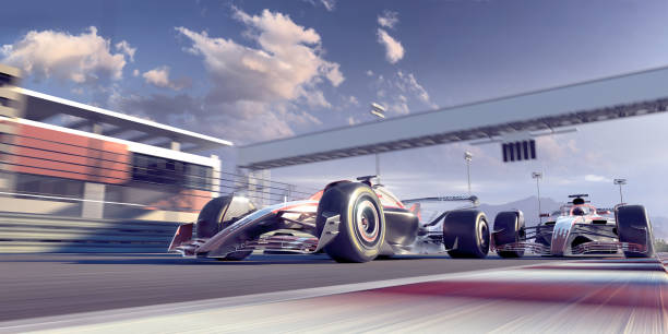 Two generic racing cars on same team driving at high speed close to each other along the finishing straight of a race track under bright sunny conditions.