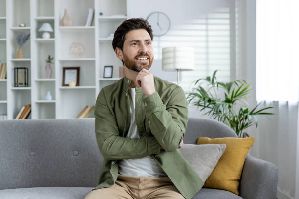 istock Smiling man thinking at home on sofa in modern living room 2157099408