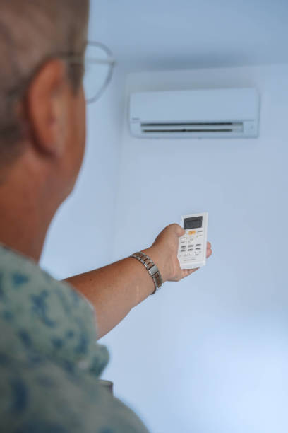 istock A man is holding a remote control in front of a wall with a white air conditione 2157099565