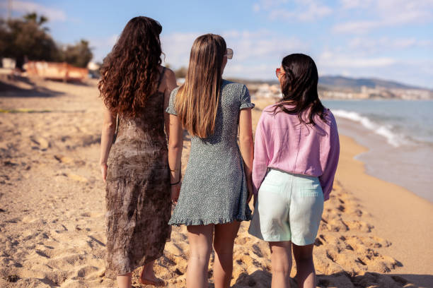 istock Rear view three female friends looking at camera on the beach having fun. 2157100995