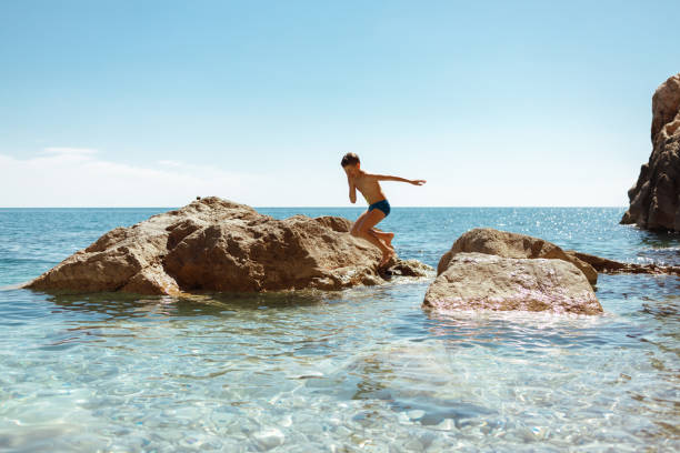 A young caucasian boy jumps from the rock to the sea in Croatia during Summer vacation.