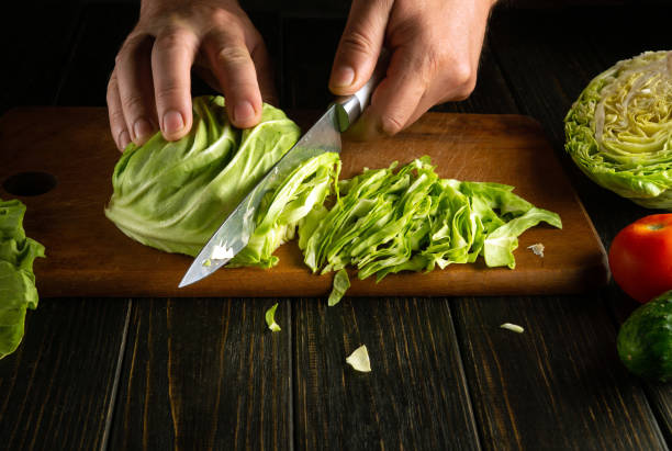 istock Cutting cabbage for preparing vegetable salad. The chef hands use a knife to chop fresh cabbage on a kitchen board. Advertising space 2157104488